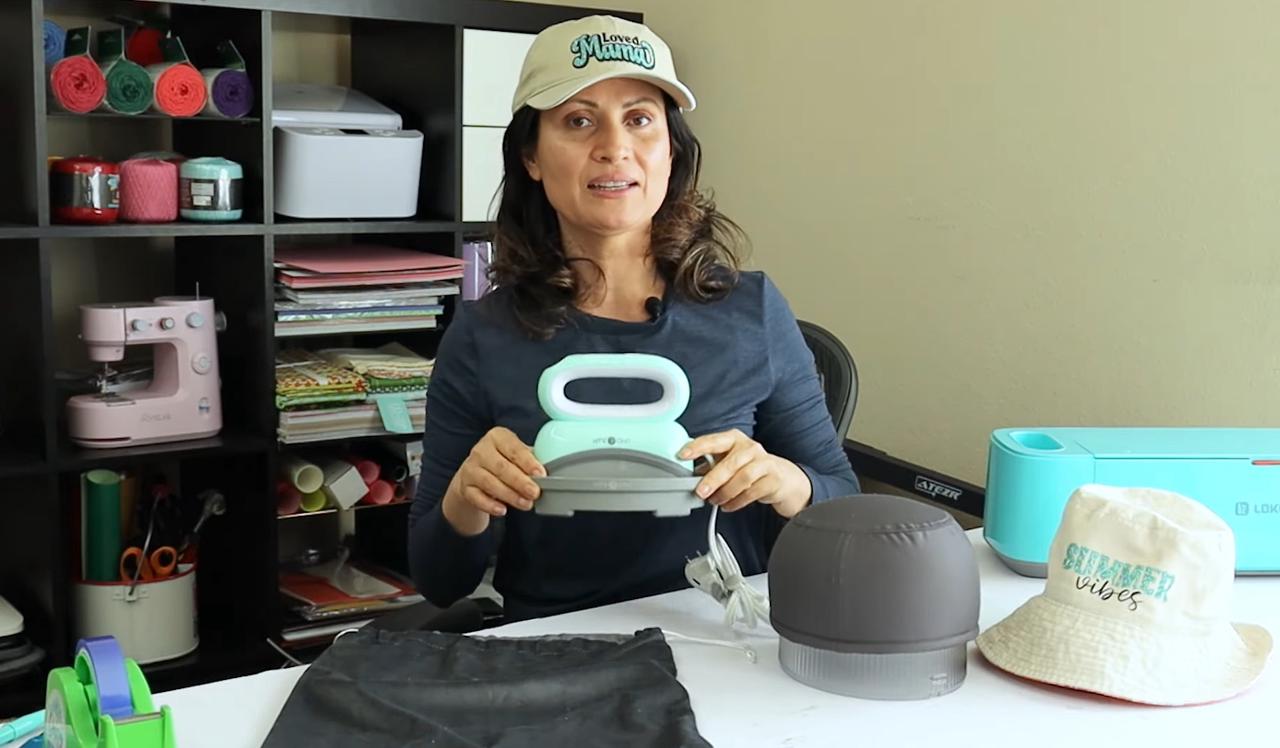 The cover image shows Daisy holding the Htvront hat heat press in both hands.
